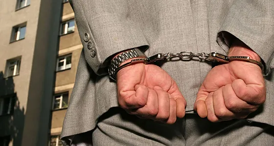 Person with hands in handcuffs in front of a building, symbolizing fast and confidential bail bond approvals in Archer Lodge, NC